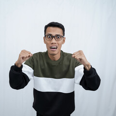 A young Asian man with glasses wearing a sweater with a happy, excited, triumphant expression while raising and clenching his fist. Isolated on white background.
