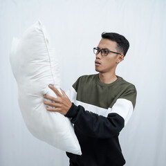 A young Asian man with glasses wearing a sweater holding and enjoying a pillow to fall asleep. Isolated on white background.