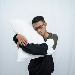 A young Asian man with glasses wearing a sweater holding and enjoying a pillow to fall asleep. Isolated on white background.