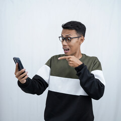 A young Asian man with glasses wearing a sweater with a surprised happy expression getting a surprise while looking at a smartphone. Isolated on a white background.
