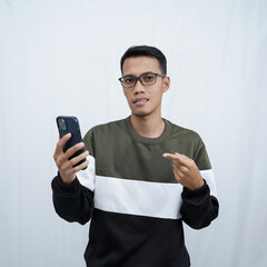 A young Asian man with glasses wearing a sweater points to a smartphone screen. Isolated on a white background.