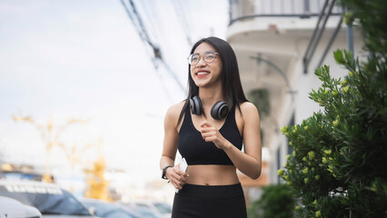 Young woman jogging in urban setting with headphones, enjoying fitness outdoors while maintaining a...