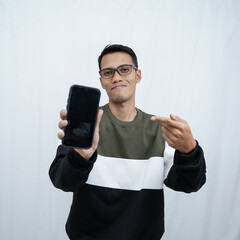 A young Asian man with glasses wearing a sweater points to a smartphone screen. Isolated on a white background.