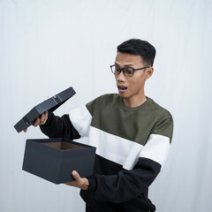 An Asian young man with glasses wearing a sweater with a surprised happy expression getting a surprise gift. Isolated on a white background.