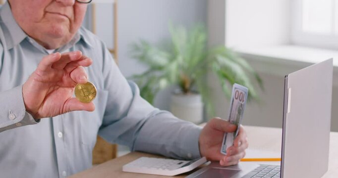 Happy elderly man sitting at a table with a laptop, holding a golden bitcoin coin and a stack of cash, celebrating crypto earnings. Financial success and online cryptocurrency transactions.