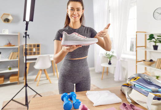 Fit sporty young woman fitness model blogger making commercial social media marketing collaboration integration with sports footwear brand, filming promotion video, holding and showing shoe at camera