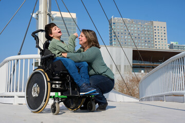 Mother hugging her son with disability in wheelchair on a bridge - cerebral palsy concept