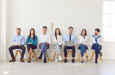 Diverse job seekers waiting for interview, female applicant hand raising sitting in queue, finding...