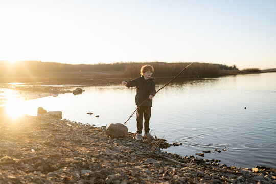 Boy 8-10 finds stick by water on clear sunny day