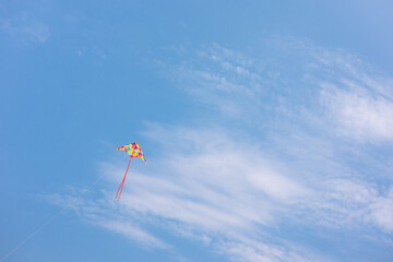Vibrant, colourful kite flying in a blue sky with white clouds