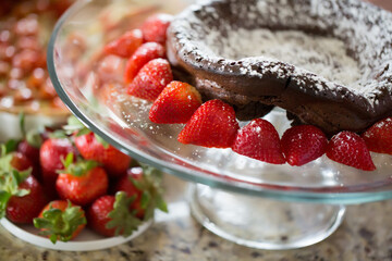 Chocolate cake with powdered sugar and strawberries on glass stand.