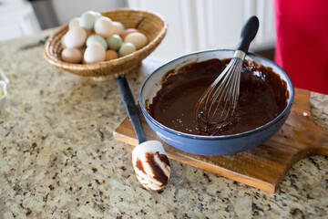 Chocolate batter with whisk and eggs on kitchen counter.