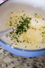 Shredded cheese and chopped chives in a mixing bowl with spoon