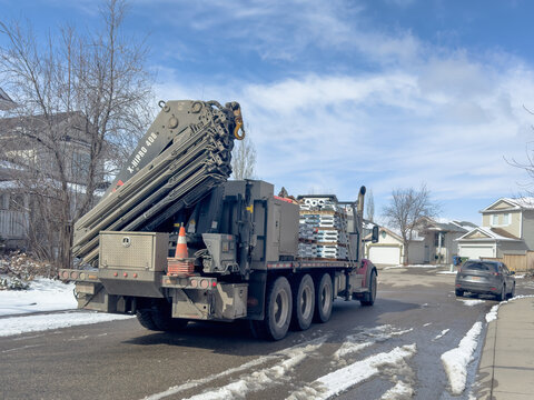 Calgary, Alberta, Canada. Apr 4, 2025. A Hiab X-HIPRO 408 crane truck parked on a residential street in a Calgary neighborhood with some snow on the ground and a partly cloudy sky.