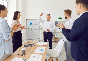 Obraz premium Happy team celebrating success and leadership. Group of young people applauding and thanking coworker for business expertise and analytics presentation at whiteboard with infographic charts and graphs