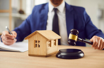 Lawyer or attorney hands holding a gavel next to a wooden house, symbolizing legal matters related to real estate, property law, foreclosure, court litigation, and legal proceedings.