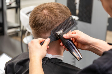 Hairdresser cutting hair of young man in barbershop, closeup shot