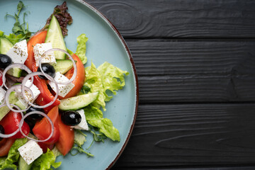 Healthy vegetable Mediterranean salad with cucumbers, tomato, olives, onion and feta cheese on dark wooden background. top view