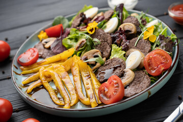 Fresh vegetable salad with grilled pepper, warm beef slices, mushrooms, balsamic glaze, lettuce, and boiled egg served on white plate. Healthy lunch concept.