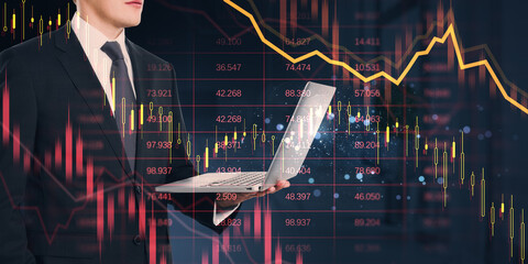 Businessman holding laptop with stock market candlestick chart overlay on dark background, financial analytics and trading concept.