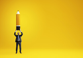 Businessman holding oversized pencil on vibrant yellow background symbolizing creativity,...