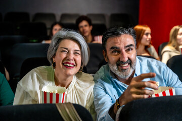 Mature couple laughing and enjoying movie at cinema with popcorn