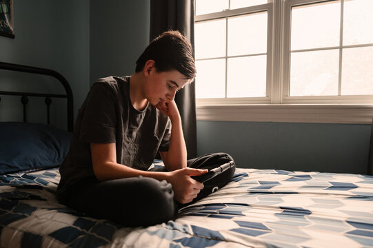 Teen boy in bedroom watching something on ipad tablet on his bed.