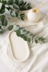 Oval Plate mockup, linen napkins, eucalyptus leaves, home fragrance diffuser top view with space...