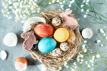 Colored chicken eggs in a nest of dry grass with feathers, rabbits and gypsophila branches on a...