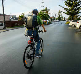 Cyclist riding on the suburb road in the morning. Houses and parked cars on the sides of the road....