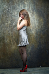 Naklejka premium A woman stands against a wall, wearing a white shirt and white stockings. She poses for a photograph, her hair long and flowing. Model in elegant clothes in a studio