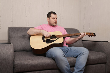 Man Playing Acoustic Guitar on Couch in Cozy Living Room Creating Relaxing Home Music Atmosphere