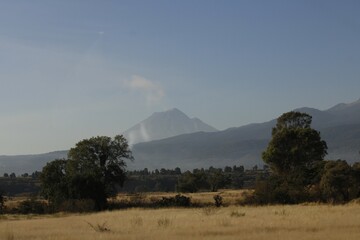 paisaje de monta&ntilde;a y colinas verdes con arboledas y arboles, llano de color amarillo y fondo de cielo azul