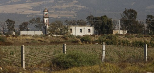 Obraz premium iglesia en medio del campo con arboles y tierras de cultivo, con fondo de colinas