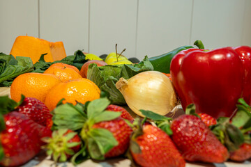 A variety of fruits and vegetables are displayed on a table, including apples, oranges, strawberries, and peppers. The arrangement of the produce creates a colorful and inviting scene