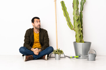Gardener man sitting on the floor at indoors having doubts while looking up