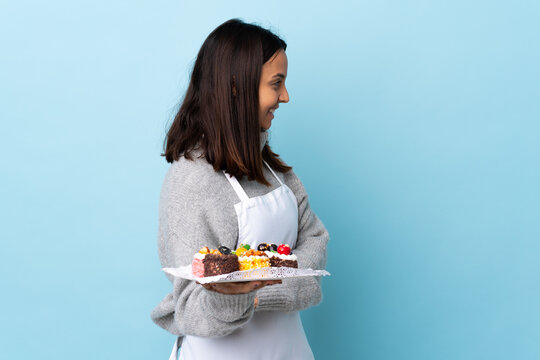 Pastry chef holding a big cake over isolated blue background in lateral position.