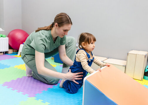 Physiotherapist assisting young child with coordination exercise in rehabilitation center. Neurological rehabilitation for child with therapeutic physiotherapy - Powered by Adobe