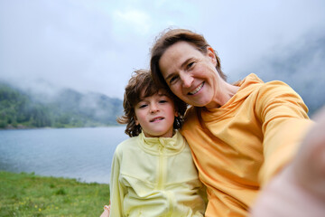 Obraz premium Happy mom and boy taking selfie against lake and mountains