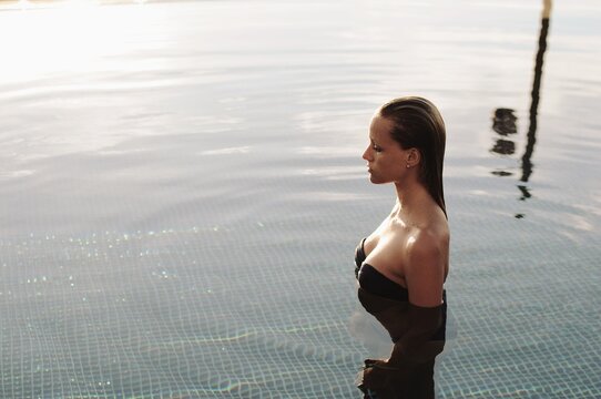 Side view of a beautiful woman in a strapless dress and long gloves standing in a swimming pool