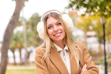 Young pretty blonde woman wearing winter muffs at outdoors keeping the arms crossed in frontal...