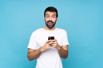 Young man with beard  over isolated blue background surprised and sending a message
