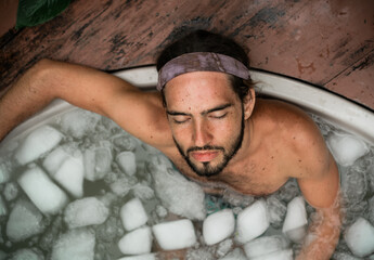 Man takes an ice bath outdoors in a lush tropical setting. Cold immersion for mental strength,...