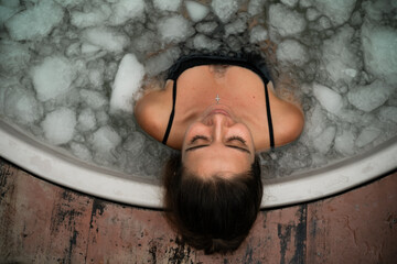 Woman practices cold therapy in an outdoor ice bath surrounded by tropical plants. A peaceful moment of self-care and healing