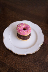 Donuts with chocolate and pink icing on a white plate on a wooden table