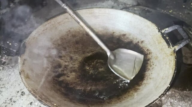 Asian cook is cooking in thai kitchen in local traditional country style, preparing  streaming vegetable oil being poured into a hot traditional wok to cooking high heat stir frying food