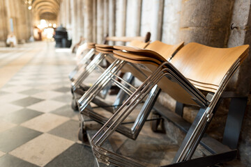 Shallow focus of a stacks of wooden chairs used by the congregation of a famous English Cathedral. Showing part of the stonework columns and tiled flooring.