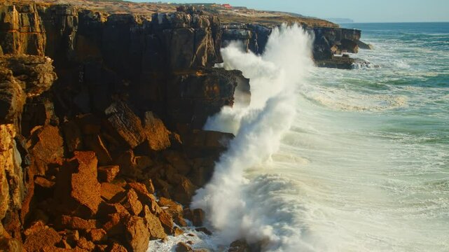 Slow motion video of huge ocean waves crashing onto the rocky shoreline in Portugal. Beautiful, big ocean waves roll onto the shore and crush on rocks. The oceanic tide at sunset.