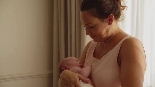 Happy mother holds a baby in her arms at sunset. A cute infant sleeps in his mother's arms. Concept of happy parenthood. Mother is rocking her newborn son in her arms. Mother and child. Slow Motion