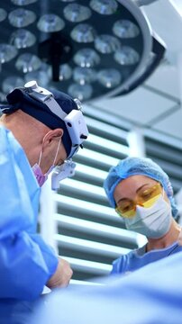 Caucasian surgeon holds the metal forceps. Female nurse assisting at operation stands at backdrop. Low angle view. Vertical video.